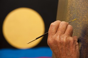 A simple device of using a finished picture hanging in the background to offset the foreground detail of the artist at work.